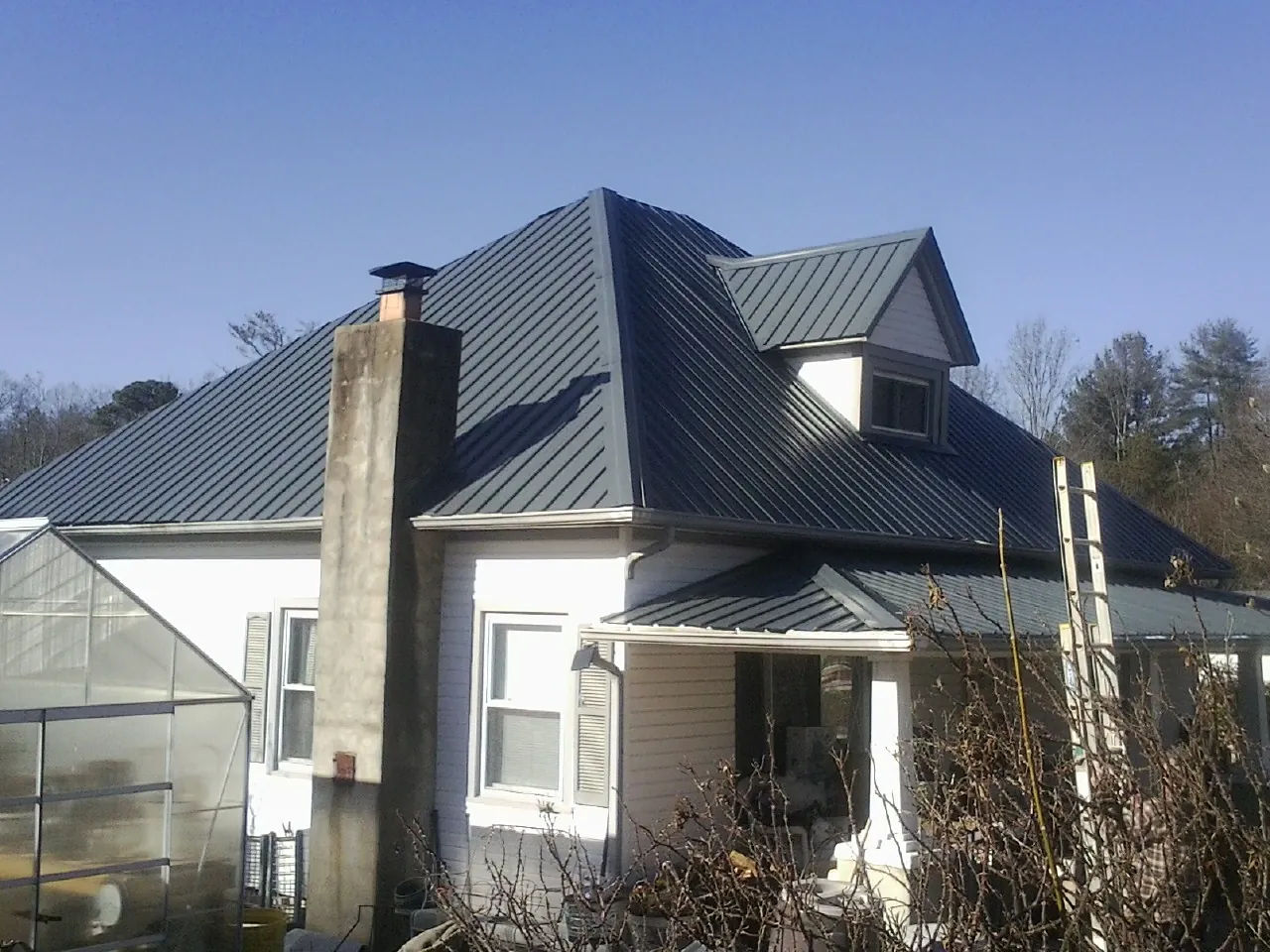 Dark blue standing seam metal roof on a white farmhouse with dormer — Slate & Tile Roof Repair by Roofing Brothers in Lewisville