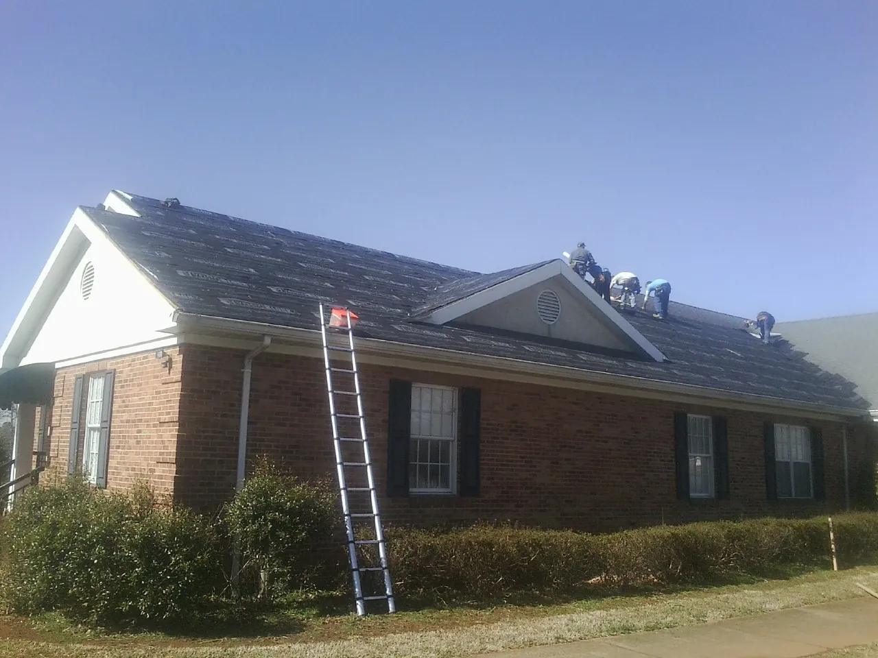 Crew tearing shingles off a brick ranch roof with a ladder set — Metal Roof Repair work by our crew in Lewisville