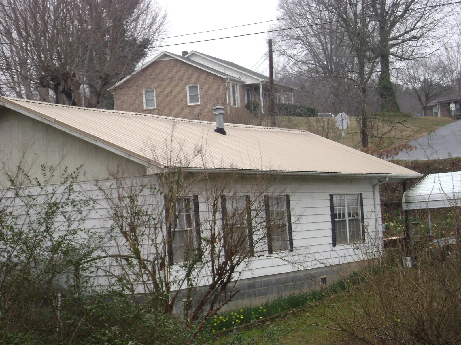 Tan metal roof on a white sided house set into a hillside — Commercial Roofing by Roofing Brothers in Lewisville